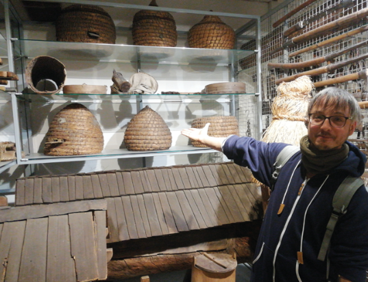 Portret Michała w Muzeum Etnograficznym na wystawie pszczelarskiej. Widać stare ule drewniane i kószki.